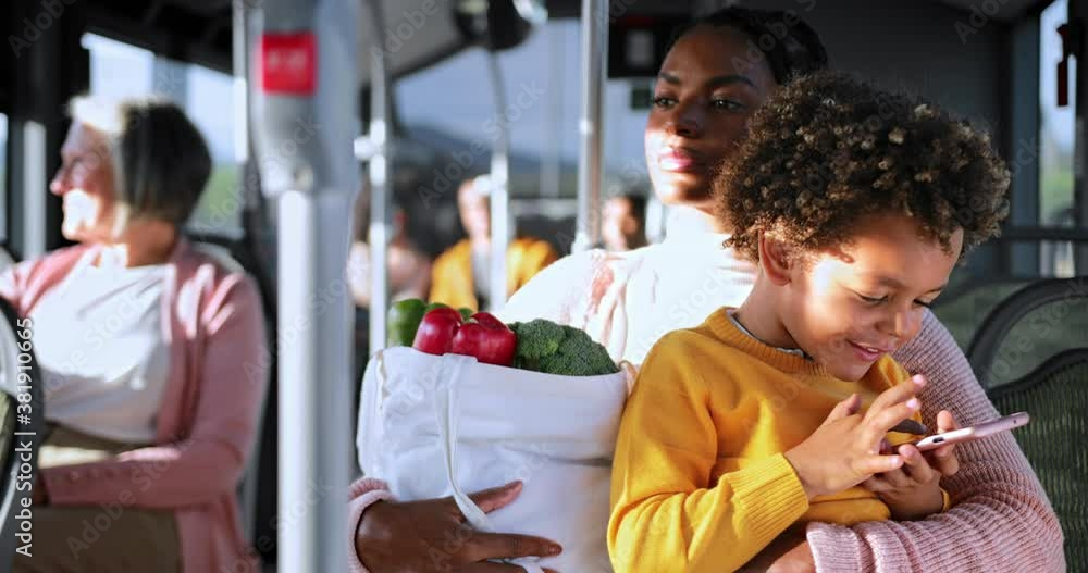 African-american mother holding groceries, son playing on smartphone inside bus African-american mother holding groceries, son playing on smartphone inside bus