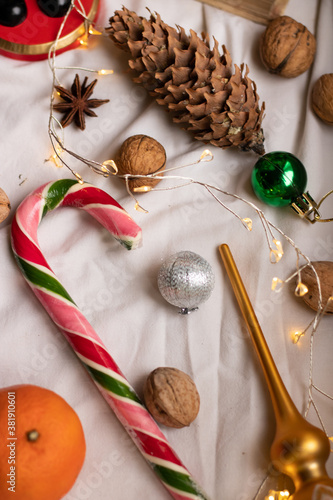 The atmosphere of Christmas and New Year. Colored caramel stick, christmas balls, walnuts, pine cone and tangerines on a light background