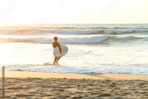surfer man with the board in his arms entering the sea at sunset