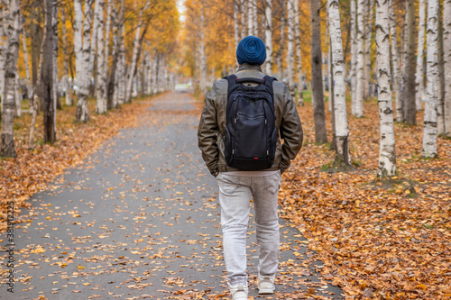 A man with a backpack walks along the alley of the autumn park.