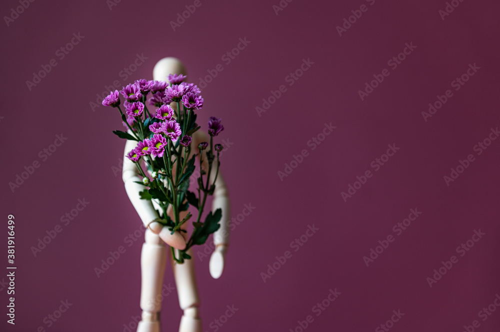 Fototapeta premium Wooden mannequin is holding tiny purple flowers like chrysanthemum, concept of giving flower bouquet to lady