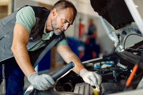 Car mechanic examining engine problems while working in repair shop.
