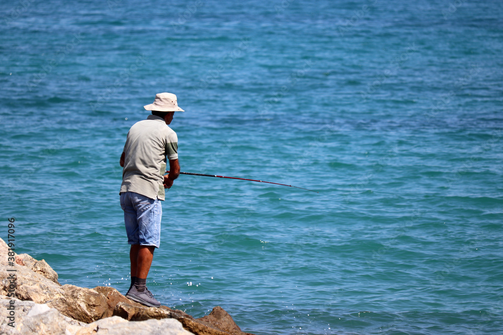 Fisherman on a rocky beach with a fishing rods, rear view. Man angling on the sea coast Fisherman on a rocky beach with a fishing rods, rear view. Man angling on the sea coast