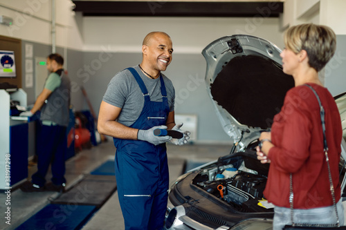 Billede på lærred Happy African American auto repairman talking to customer in a workshop