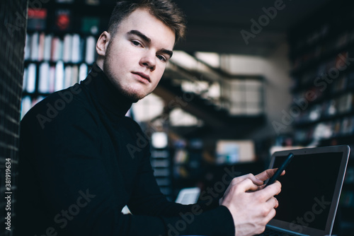 Serious young man using smartphone and laptop