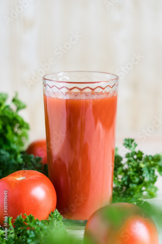 Fresh tomato juice in glass with parsley and ripe tomatoes on light wooden table. Selective focus