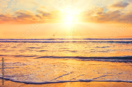 The golden light rays of the sun illuminates the morning beach on the ocean coast.
