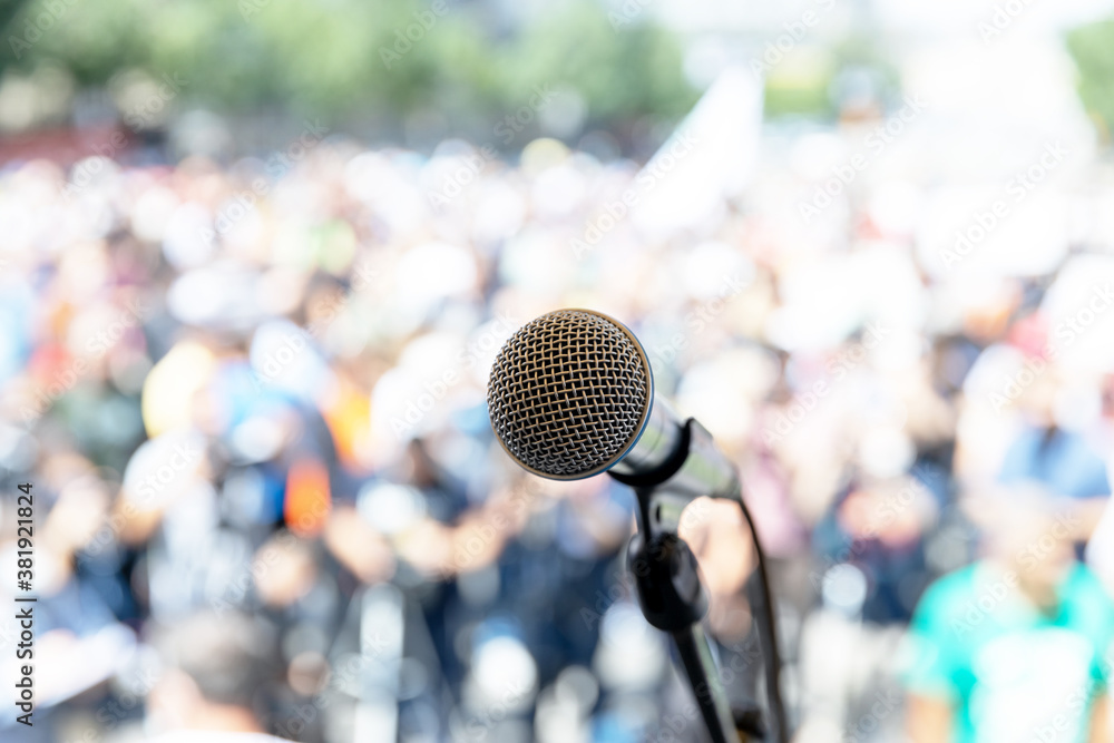 Focus on microphone, blurred group of people at mass protest in the background Focus on microphone, blurred group of people at mass protest in the background