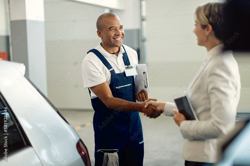 Obraz premium Happy African American mechanic handshaking with businesswoman in auto repair shop.