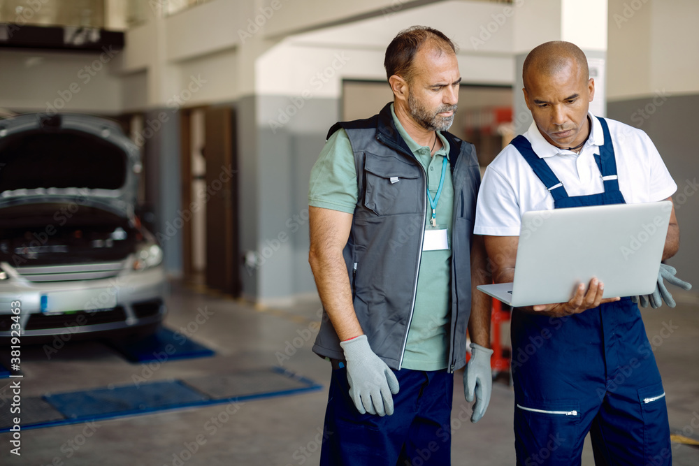 Fototapeta premium Auto repairmen cooperating while working on laptop at car service workshop.