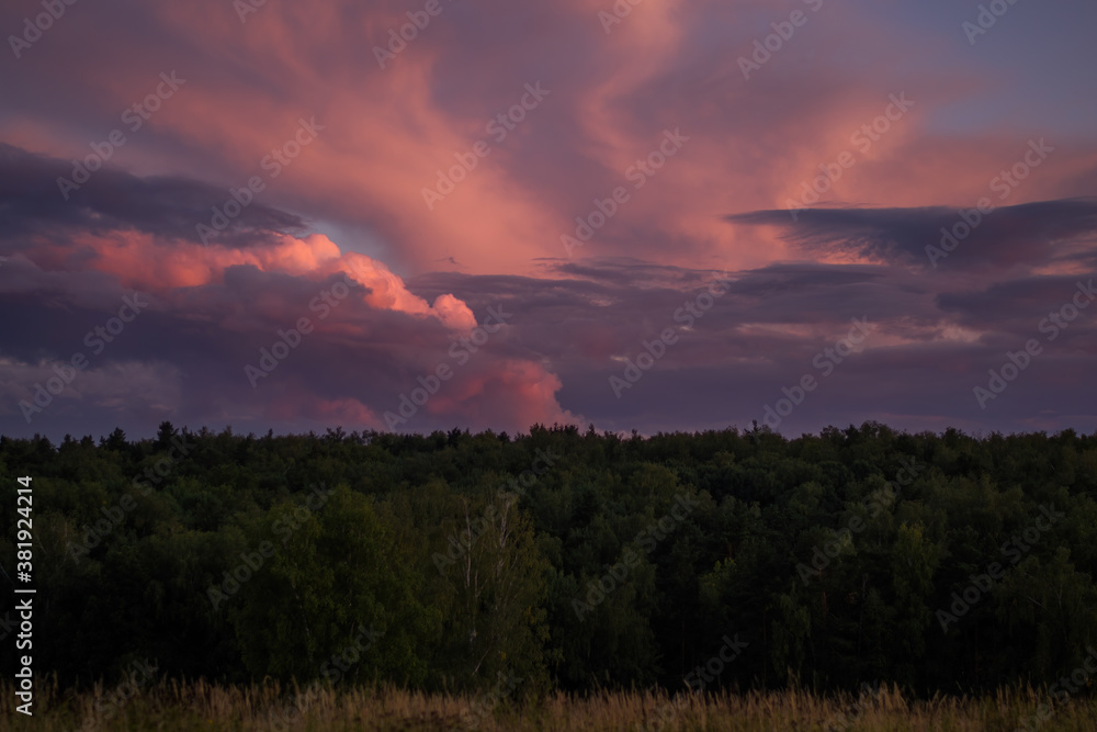 There are dramatic clouds in the dark sky as the sun sets. The sky is dominated by fuchsia, pink. There are dramatic clouds in the dark sky as the sun sets. The sky is dominated by fuchsia, pink.