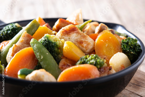 Stir fry chicken with vegetables on iron pan on wooden table. Close up 