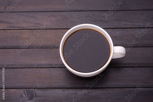 Dark coffee in a white coffee cup is placed on a black wooden table and has a space for designing messages.