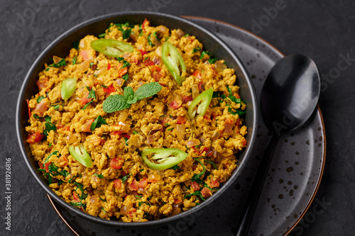 Masala Egg Bhurji or Muttai Podimas in black bowl on dark slate table top. Anda Bhurji is indian cuisine scrambled eggs dish with spices. Asian food and meal.