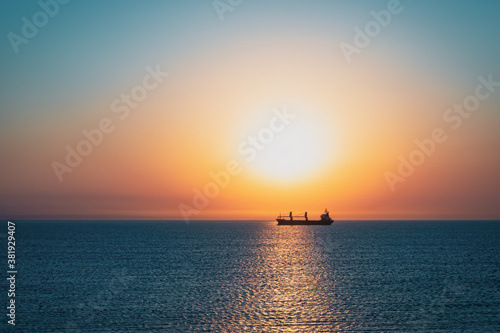 Rising sun over blue sea and silhouette of a transport ship © SerPhoto