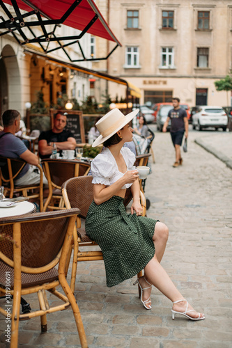 beautiful stylish young woman in a hat sitting at a table in a cafe and drinking coffee