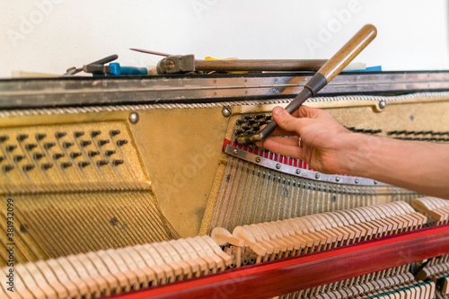 Piano tuning process. closeup of hand and tools of tuner working on grand piano. Detailed view of Upright Piano during a tuning