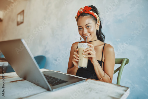 Obraz na płótnie a young mixed race woman drink iced coffee and using her laptop in cafe w salonie