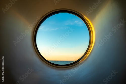 Sunset ocean view of horizon seen from inside of a cruise ship cabin through a round circular window.