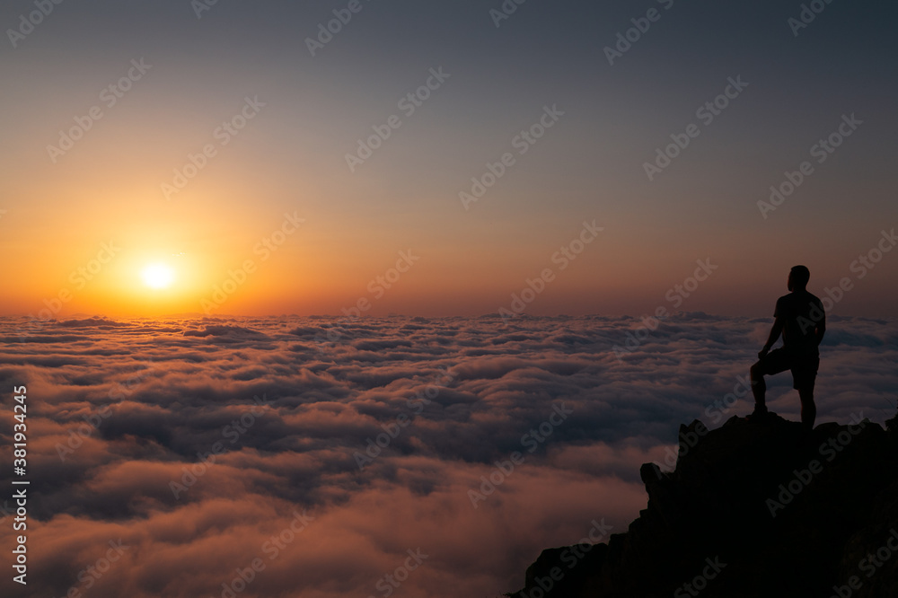 Sunset Silhouette of a person over the Clouds standing on a mountain top