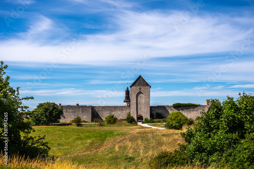 Beautiful rural summer view of an ancient medieval brick tower and defense wall surrounding the city of Visby Gotland, Sweden. Blue sky and grassy fields.