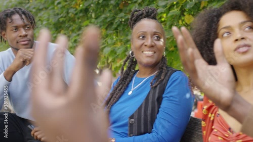 Group of 4 black friends sitting together in conversation on a bench outside, in slow motion