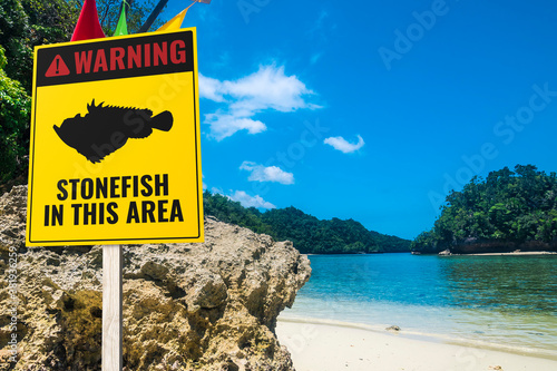 A stonefish warning sign at a rocky beach. A stern warning for barefoot bathers. Tropical beach setting. photo