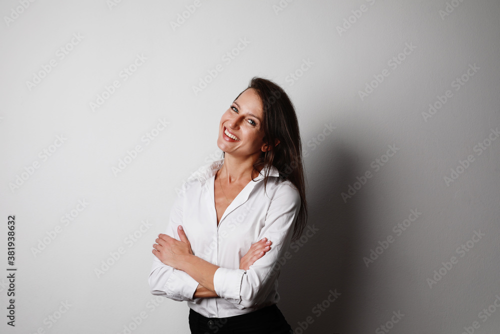 Portrait of young smiling dark-haired woman wearing white blouse posing against white background. Space for text. Portrait of young smiling dark-haired woman wearing white blouse posing against white background. Space for text.