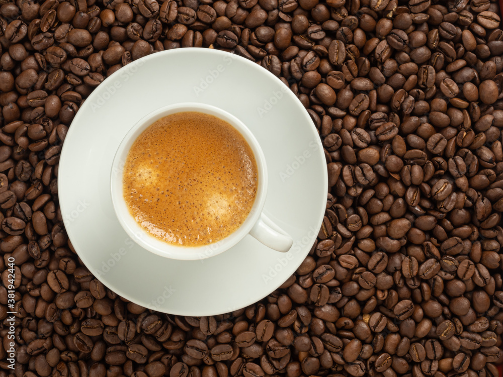 Fototapeta premium white cup with coffee, stands on coffee beans in soft focus, top view, copy space