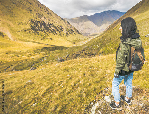 Young woman traveler stands on the rock and enjoys scenic views of Juta valley in Kazbegi national park.