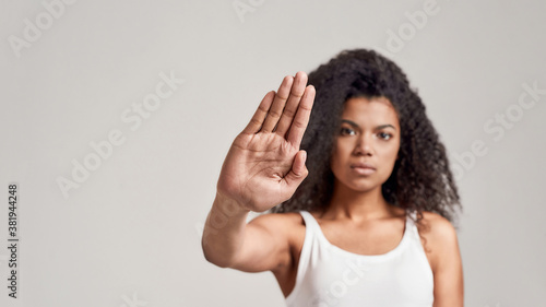 Portrait of young african american woman with curly hair wearing white shirt having serious confident look while showing, making stop gesture isolated over grey background