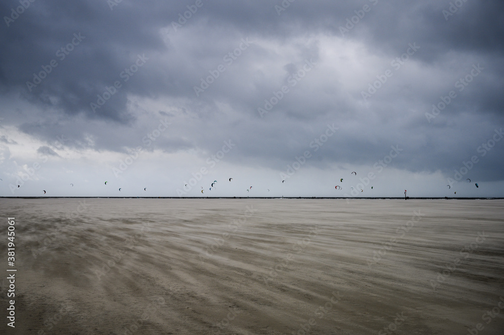 large beach with many kite surfers in the background with stormy sky large beach with many kite surfers in the background with stormy sky