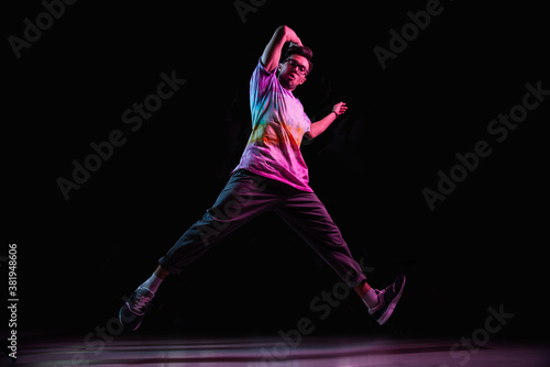 Professional break dancer jumping, practicing modern hip-hop dance in pink neon light
