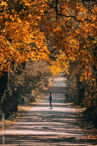 Young sporty woman riding on the skateboard on the road. Aerial view of road in autumn with colorful trees.