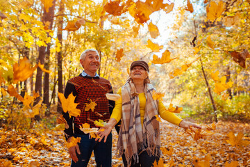 Fall season. Family couple throwing leaves in autumn forest. Senior people having fun outdoors enjoying nature