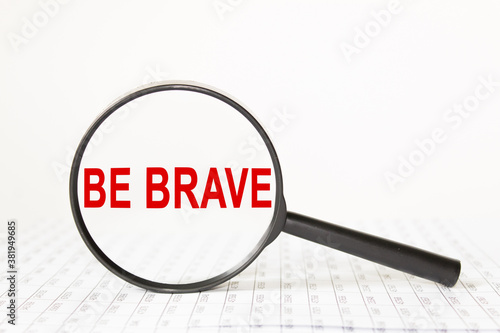 words be brave in a magnifying glass on a white background. business concept © Valeria