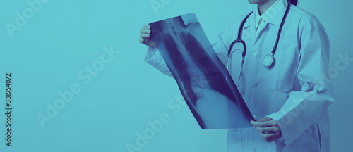 Middle aged of asian woman doctor standing and holding a x-ray film or radiography. she looking for unnormal or disease on lungs which illness from coronavirus pandemic.