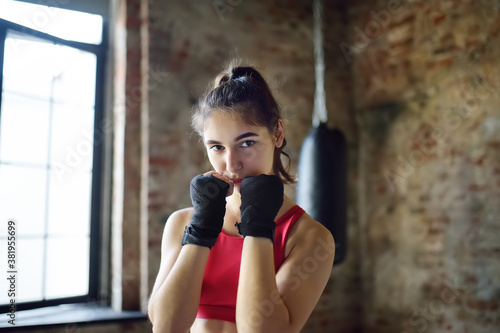 Young woman ready for hits punching bag during a boxing training. Female boxer doing fitness.