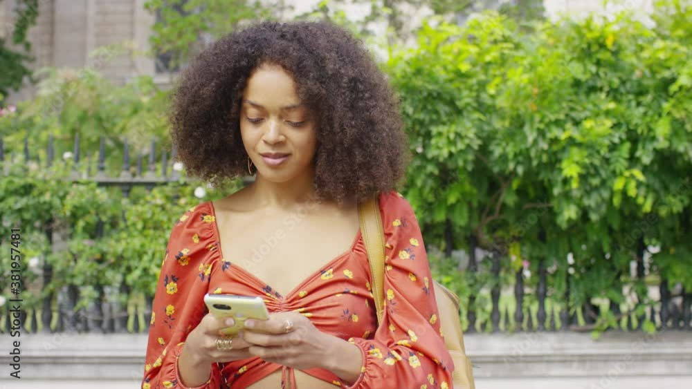Young woman smiles to herself as she walks and uses her phone in the city, in slow motion Young woman smiles to herself as she walks and uses her phone in the city, in slow motion