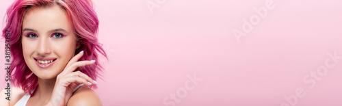 young woman with colorful hair and makeup posing with hand near face isolated on pink, panoramic shot
