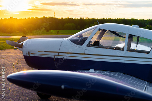 Close-up of a small parked plane with a propeller against the backdrop of a sunset.