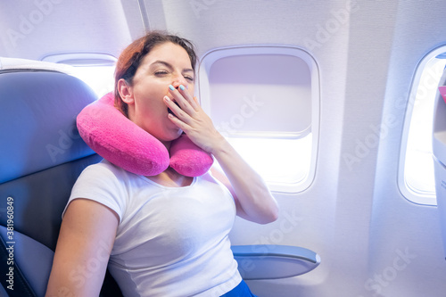 Woman yawns while sitting on the plane by the window.
