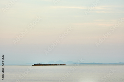A desolate island stands proudly in the middle of the Atlantic Ocean off the Isle of Mull, Scotland. The Isle of Jura mountains can be seen in the background. Muted tones create a relaxing photo
