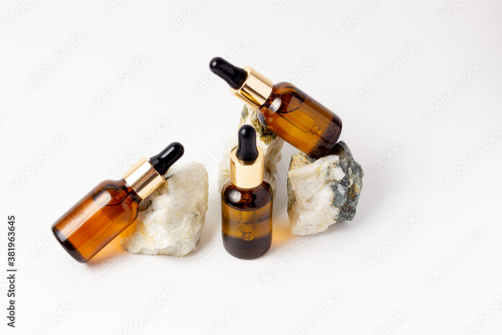 Natural cosmetics in glass bottles with a dropper stand next to a stone on a beige background with bright sunlight. The concept of natural cosmetics, natural essential oil Natural cosmetics in glass bottles with a dropper stand next to a stone on a beige background with bright sunlight. The concept of natural cosmetics, natural essential oil
