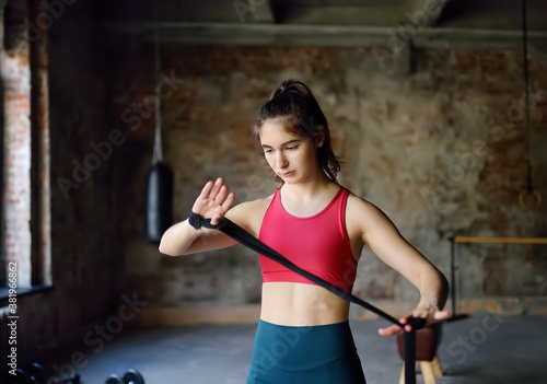 Young female boxer preparing for boxing fight. Athletic woman wearing strap on wrist before boxing practice in gym.