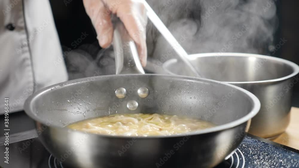 Boiling risotto in slow motion. White smoke rising above hot frying pan on dark background. Cooking in restaurant. Delicious risotto being cooked in kitchen. Full hd Boiling risotto in slow motion. White smoke rising above hot frying pan on dark background. Cooking in restaurant. Delicious risotto being cooked in kitchen. Full hd