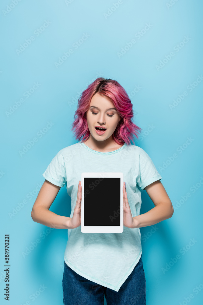 excited young woman with pink hair presenting digital tablet with blank screen on blue background excited young woman with pink hair presenting digital tablet with blank screen on blue background