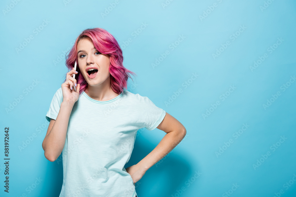 young woman with pink hair talking on smartphone with open mouth on blue background young woman with pink hair talking on smartphone with open mouth on blue background