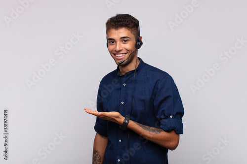 young telemarketer man smiling cheerfully, feeling happy and showing a concept in copy space with palm of hand