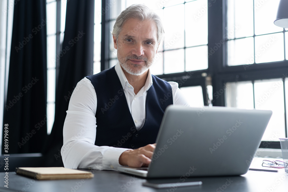 Concentrated at work. Happy mature man in full suit using laptop while working in modern office Concentrated at work. Happy mature man in full suit using laptop while working in modern office